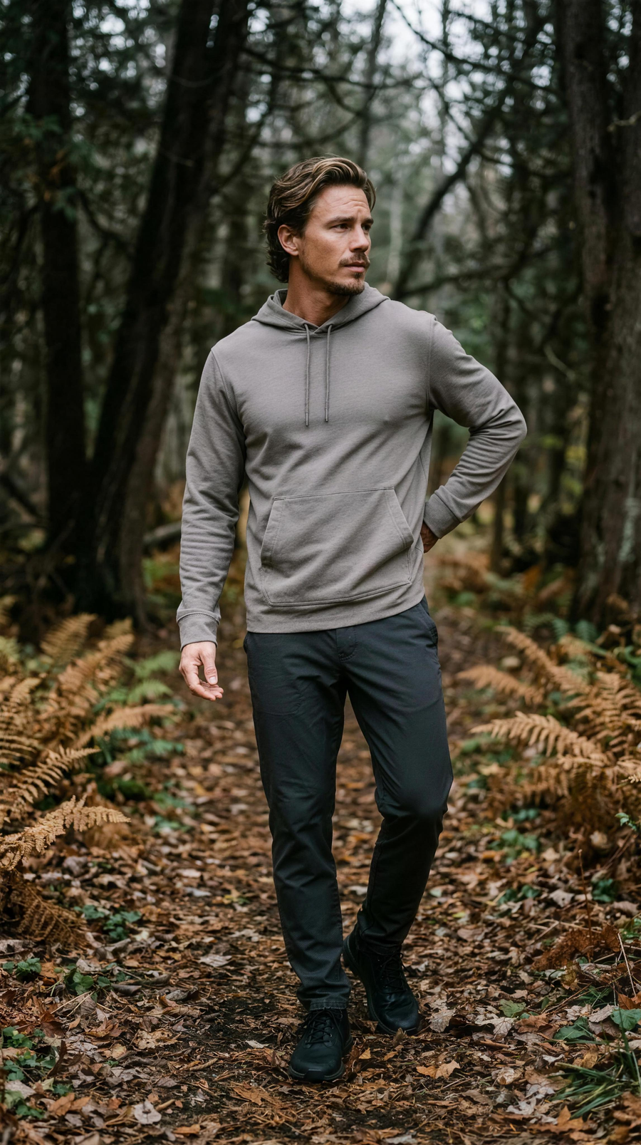 Ten Thousand Waterproof Hoodie in Flat Dark Earth, hood down, worn with charcoal trousers on a cedar forest trail in Door County, Wisconsin, late October.