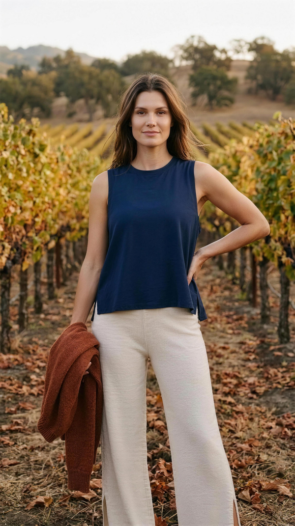 Serene Tank - Navy Blue — Napa: front view of the loose swingy navy crew-neck tank with its broad shoulders and side slits, worn untucked over cream wide-leg trousers with a rust knit carried, in the turning vine rows