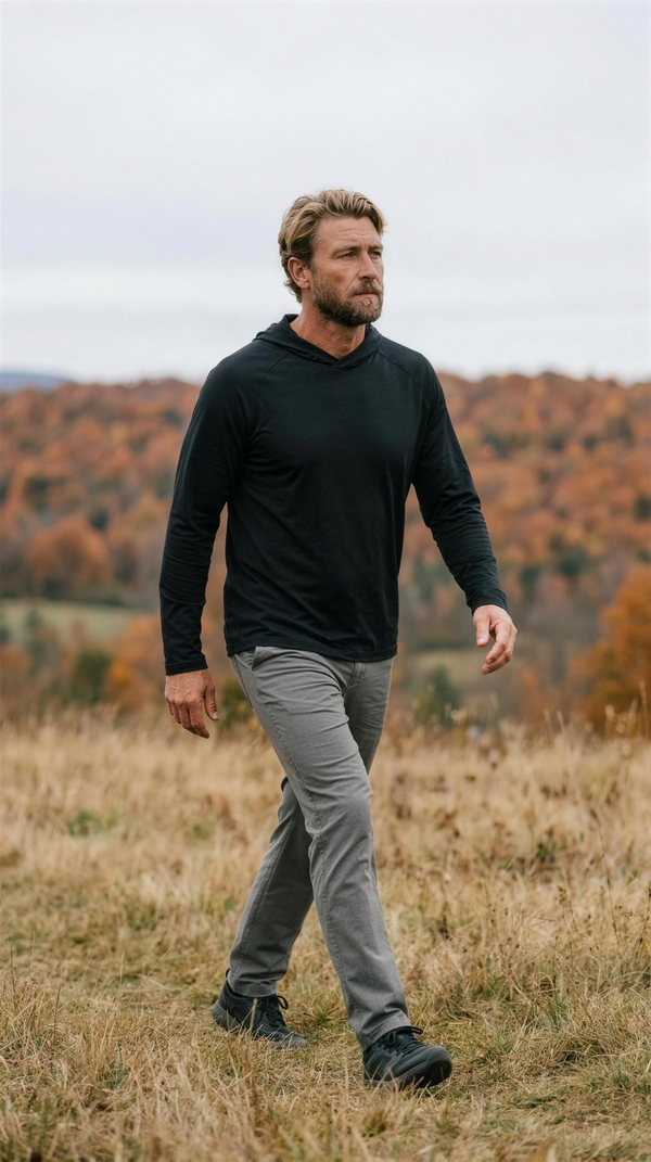 Ten Thousand Tactical Hooded Shirt in black, worn with stone-grey technical trousers on an open hillside meadow near Stowe, Vermont, mid-October.