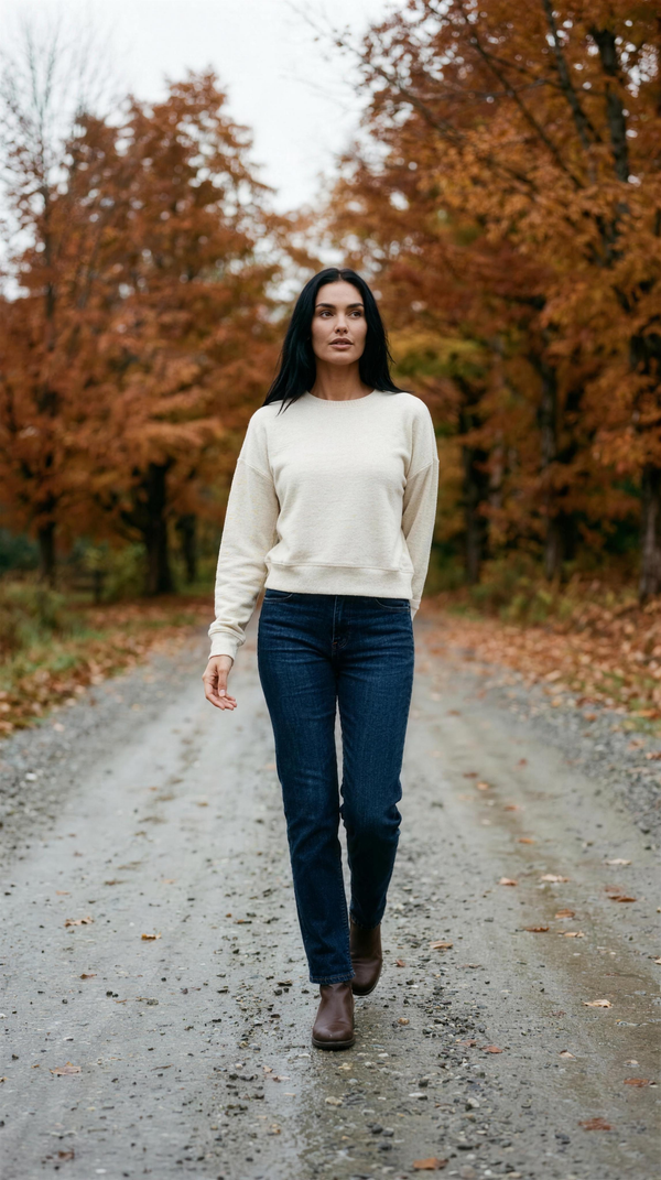 TravisMathew Cloud Terry Crew in Heather Natural with dark indigo denim, walking a wet gravel track through a maple stand outside Stowe, Vermont in mid-October.
